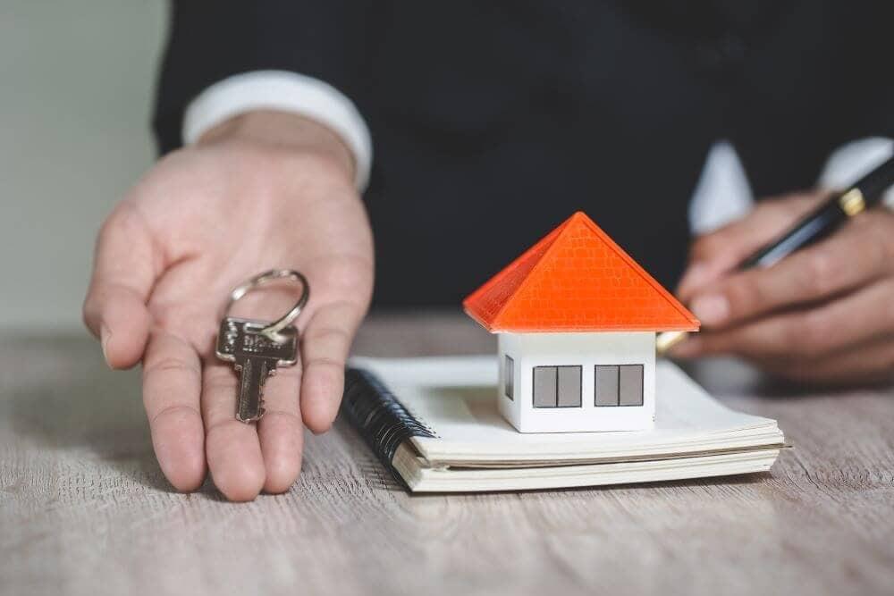 Hand holding keys, house model nearby.
